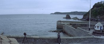 Movie still from “The Eagle Has Landed” (1976), directed by John Sturges – A person standing on the side of a pier near the ocean; Extreme Wide shot, High angle