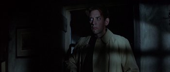 Movie still from “The Eagle Has Landed” (1976), directed by John Sturges – A man wearing a suit and tie standing in a dark room; Close Up shot, Over the shoulder angle