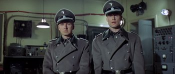 Movie still from “The Eagle Has Landed” (1976), directed by John Sturges – A couple of men in uniforms standing next to each other; Medium shot, Low angle