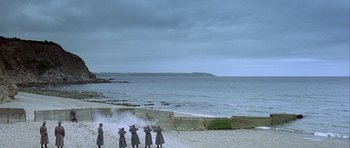 Movie still from “The Eagle Has Landed” (1976), directed by John Sturges – A group of people standing on top of a sandy beach next to the ocean; Extreme Wide shot, High angle