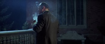 Movie still from “The Eagle Has Landed” (1976), directed by John Sturges – A man smoking a cigarette while wearing a suit; Medium shot, Over the shoulder angle