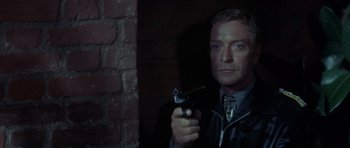 Movie still from “The Eagle Has Landed” (1976), directed by John Sturges – A man holding a gun while standing next to a brick wall; Close Up shot, Low angle