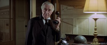 Movie still from “The Eagle Has Landed” (1976), directed by John Sturges – An older man in a suit and tie holding a phone; Close Up shot, Low angle