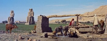 Movie still from “The Egyptian” (1954), directed by Michael Curtiz – A woman standing next to a stone structure; Wide shot, Low angle