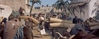 Movie still from “The Egyptian” (1954), directed by Michael Curtiz – A group of people standing next to each other on a dirt road; Wide shot, High angle
