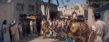 Movie still from “The Egyptian” (1954), directed by Michael Curtiz – A group of men in ancient egyptian costumes marching down a street; Wide shot, High angle