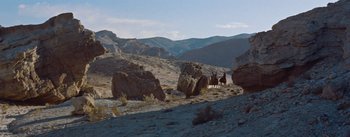 Movie still from “The Egyptian” (1954), directed by Michael Curtiz – Two people riding horses in the desert near some boulders; Extreme Wide shot, High angle