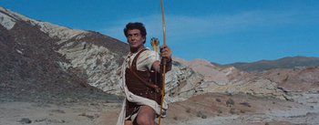 Movie still from “The Egyptian” (1954), directed by Michael Curtiz – A man holding a bow and arrow while standing on a hill; Medium shot, Low angle