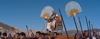Movie still from “The Egyptian” (1954), directed by Michael Curtiz – An old man sitting in a chair on top of a boat; Wide shot, Low angle