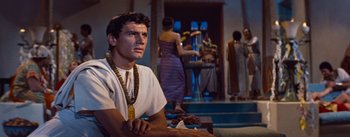 Movie still from “The Egyptian” (1954), directed by Michael Curtiz – A man sitting on the ground in front of people; Medium shot, Over the shoulder angle