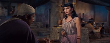 Movie still from “The Egyptian” (1954), directed by Michael Curtiz – A woman in a purple dress is talking to an older man; Medium shot, Over the shoulder angle