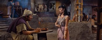 Movie still from “The Egyptian” (1954), directed by Michael Curtiz – A woman standing next to a man holding a knife; Medium shot, Over the shoulder angle