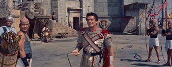 Movie still from “The Egyptian” (1954), directed by Michael Curtiz – A man dressed as a roman centurion holding a nintendo wii game controller; Medium shot, High angle