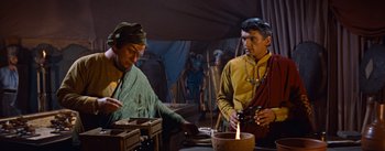 Movie still from “The Egyptian” (1954), directed by Michael Curtiz – A man and a woman standing next to each other in front of a fire; Medium shot, Over the shoulder angle