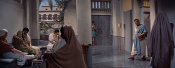 Movie still from “The Egyptian” (1954), directed by Michael Curtiz – A woman in a brown robe sitting in front of a building; Wide shot, High angle