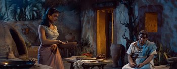 Movie still from “The Egyptian” (1954), directed by Michael Curtiz – A woman standing next to a table with food on top of it; Medium shot, Low angle