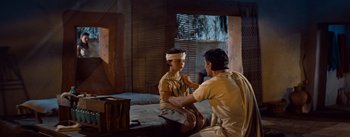 Movie still from “The Egyptian” (1954), directed by Michael Curtiz – A man is bandaging a young boy's head; Medium shot, Over the shoulder angle