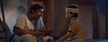 Movie still from “The Egyptian” (1954), directed by Michael Curtiz – A man and a boy are talking to each other; Medium shot, Over the shoulder angle