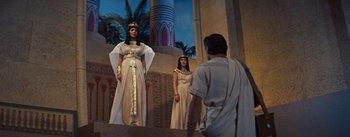 Movie still from “The Egyptian” (1954), directed by Michael Curtiz – Two women dressed as cleopatra and a man in egyptian garb stand in front of a building; Wide shot, Low angle