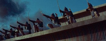 Movie still from “The Egyptian” (1954), directed by Michael Curtiz – A group of men holding bows and arrows on top of a building; Wide shot, Low angle