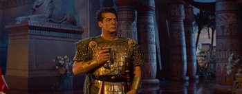 Movie still from “The Egyptian” (1954), directed by Michael Curtiz – A man dressed as a roman centurion holding a sword; Medium shot, Over the shoulder angle
