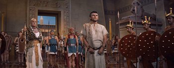 Movie still from “The Egyptian” (1954), directed by Michael Curtiz – A group of men in ancient roman garb standing next to each other in front of a building; Wide shot, Low angle