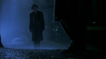 Movie still from “The End of the Affair” (1999), directed by Neil Jordan – A man in a hat and a coat standing in the dark; Wide shot, Low angle