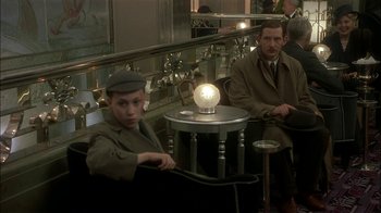 Movie still from “The End of the Affair” (1999), directed by Neil Jordan – Two men sitting at a table with a lamp on top of it; Medium shot, Over the shoulder angle