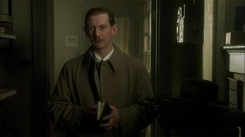 Movie still from “The End of the Affair” (1999), directed by Neil Jordan – A man in a brown coat holding a book; Close Up shot, Low angle