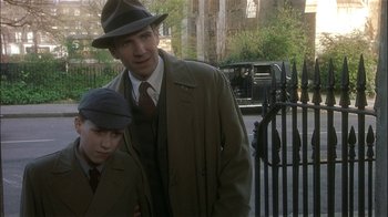 Movie still from “The End of the Affair” (1999), directed by Neil Jordan – A man and a young boy standing next to each other in front of a gate; Medium shot, Over the shoulder angle