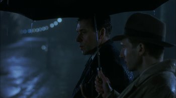 Movie still from “The End of the Affair” (1999), directed by Neil Jordan – A man holding an umbrella while standing next to another man; Close Up shot, Over the shoulder angle