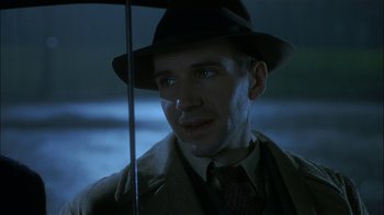 Movie still from “The End of the Affair” (1999), directed by Neil Jordan – A man in a hat and coat holding an open umbrella; Close Up shot, Over the shoulder angle