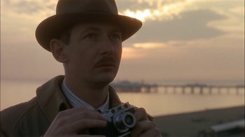 Movie still from “The End of the Affair” (1999), directed by Neil Jordan – A man with a hat and a camera in front of a body of water; Close Up shot, Low angle