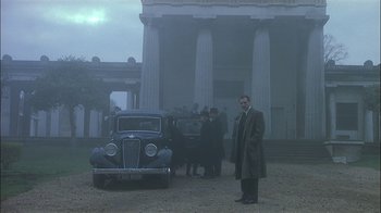 Movie still from “The End of the Affair” (1999), directed by Neil Jordan – A man standing in front of an antique car; Wide shot, Low angle