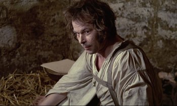 Movie still from “The Enigma of Kaspar Hauser” (1974), directed by Werner Herzog – A man sitting in a barn looking to his left; Medium shot, High angle