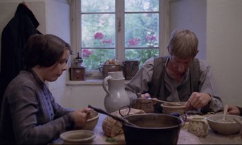 Movie still from “The Enigma of Kaspar Hauser” (1974), directed by Werner Herzog – Two people sitting at a table with a bowl of food; Medium shot, Low angle