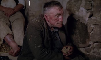 Movie still from “The Enigma of Kaspar Hauser” (1974), directed by Werner Herzog – An older man holding a piece of food in his hands; Medium shot, High angle
