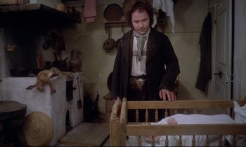 Movie still from “The Enigma of Kaspar Hauser” (1974), directed by Werner Herzog – A man standing next to a baby in a wooden crib; Medium shot, High angle