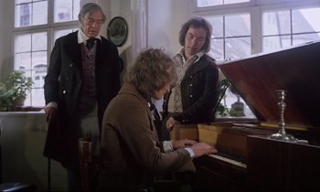 Movie still from “The Enigma of Kaspar Hauser” (1974), directed by Werner Herzog – A man sitting at a piano in front of two other men; Medium shot, High angle