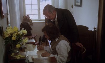 Movie still from “The Enigma of Kaspar Hauser” (1974), directed by Werner Herzog – A man standing next to a woman writing on a paper; Medium shot, High angle