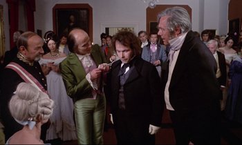 Movie still from “The Enigma of Kaspar Hauser” (1974), directed by Werner Herzog – A group of people standing in a room; Medium shot, Over the shoulder angle