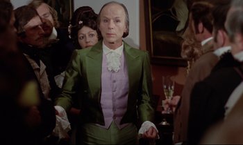 Movie still from “The Enigma of Kaspar Hauser” (1974), directed by Werner Herzog – An older man in a green and purple suit; Medium shot, Over the shoulder angle