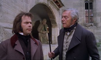 Movie still from “The Enigma of Kaspar Hauser” (1974), directed by Werner Herzog – Two men standing next to each other in front of a statue; Medium shot, Over the shoulder angle