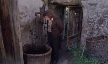 Movie still from “The Enigma of Kaspar Hauser” (1974), directed by Werner Herzog – A man standing next to an old wooden barrel; Wide shot, High angle