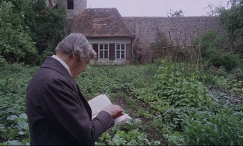 Movie still from “The Enigma of Kaspar Hauser” (1974), directed by Werner Herzog – An older man reading a book in a garden; Medium shot, Over the shoulder angle