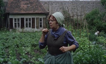 Movie still from “The Enigma of Kaspar Hauser” (1974), directed by Werner Herzog – An old woman in a field with a house in the background; Medium shot, Over the shoulder angle