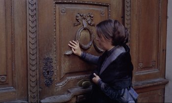 Movie still from “The Enigma of Kaspar Hauser” (1974), directed by Werner Herzog – A woman touching a door knob on a wooden door; Medium shot, High angle