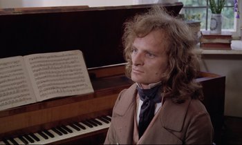 Movie still from “The Enigma of Kaspar Hauser” (1974), directed by Werner Herzog – A man in a brown jacket and a tie sitting in front of a piano; Medium shot, High angle