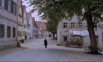 Movie still from “The Enigma of Kaspar Hauser” (1974), directed by Werner Herzog – A person walking down a street near some buildings; Extreme Wide shot, High angle