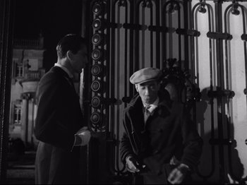 Movie still from “The Exterminating Angel” (1962), directed by Luis Buñuel – Two men standing next to each other in front of an iron gate; Medium shot, Low angle